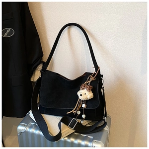 Detail of black suede shoulder bag with cute teddy bear charm on a metallic suitcase