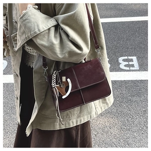Detail of burgundy crossbody bag featuring white stitching and horse charm ornament