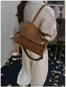 Brown suede crossbody bag detail showing plush bear charm and vintage tassel on wide strap