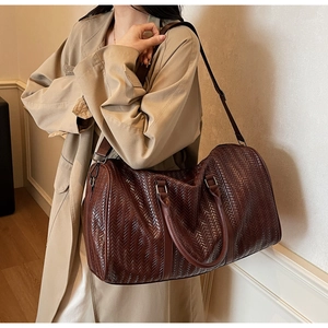Détail d'un sac de voyage tressé marron foncé porté par un mannequin en trench-coat