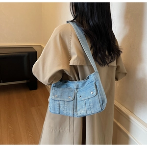 Détail du sac bandoulière en denim bleu clair avec boucles métal et poches à rabat
