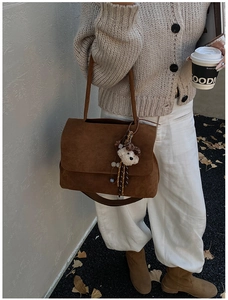 Detail view of large brown suede crossbody bag with leopard print bear charm for commute