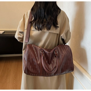 Détail d'un sac de voyage marron foncé tissé porté avec un trench-coat beige