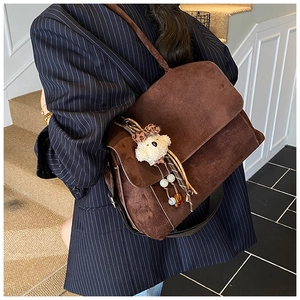 Side view of a vintage brown suede shoulder bag with a cute plush bear charm on a model