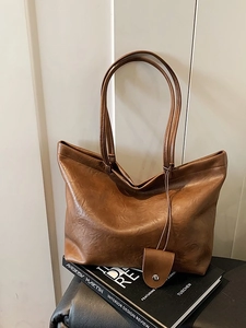 Minimalist brown leather tote bag with long straps and charm in a lifestyle setting