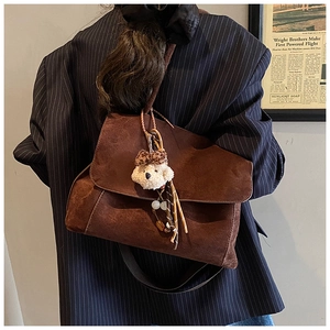 Brown suede crossbody bag detail with plush bear charm and woven tassel accent