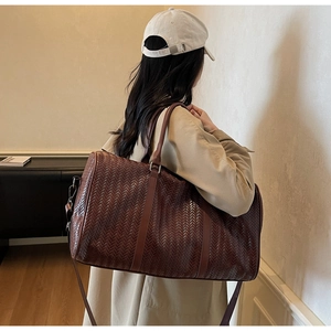 Gros plan du sac de voyage tressé marron montrant la texture et la bandoulière amovible