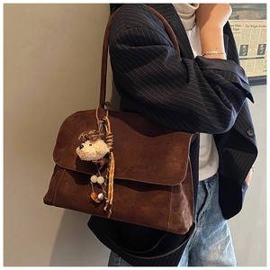 Detail of brown suede shoulder bag with plush poodle charm and crossbody strap