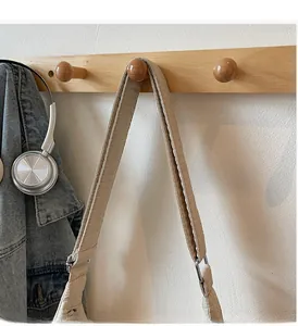 Detail of a padded cream tote bag strap with quilted texture hanging on a wooden hook