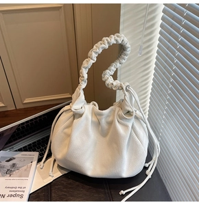 Detail der cremefarbenen Cord-Eimertasche mit Faltenstruktur und geflochtenem Griff