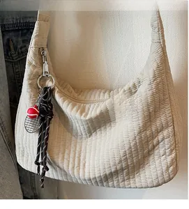 Detail of cream quilted hobo bag with striped texture and sporty tennis racket charm