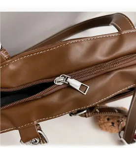 Détail de la fermeture éclair argentée sur sac en daim marron avec surpiqûres blanches