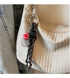Detail of a mini tennis racket keychain accessory on a quilted beige tote bag