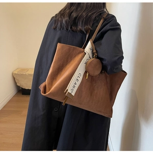 Detail of a brown suede tote bag featuring a round coin purse and decorative lettered strap