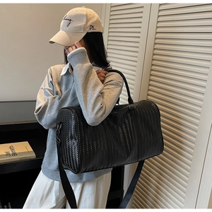 Détail de la texture tressée noire d'un grand sac de voyage avec finition cuir et bandoulière