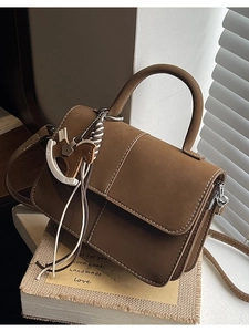 Brown crossbody handbag with contrast stitching and horse charm on a book background