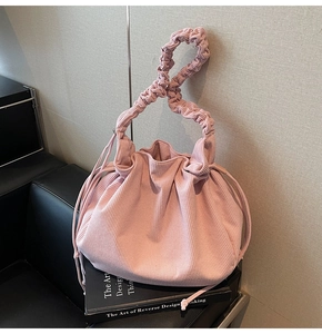 Detailaufnahme der rosa Cord-Faltenhandtasche mit gerafftem Griff auf einem Designbuch
