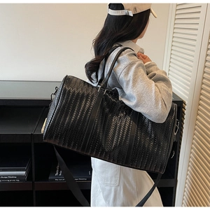 Détail d'un sac de voyage tressé noir avec bandoulière réglable porté par un mannequin