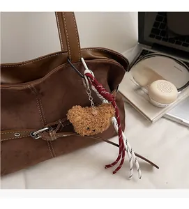 Détail d'un joli charme ours en peluche marron avec chaîne sur un sac fourre-tout en daim