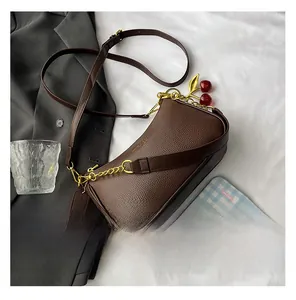 Détail du sac en cuir grainé marron foncé avec chaîne dorée et breloque cerise