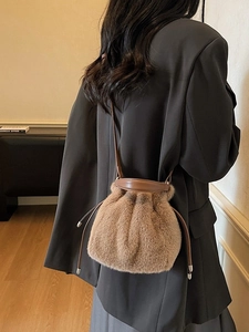 Brown plush faux fur bucket bag with leather drawstring strap worn by a female model