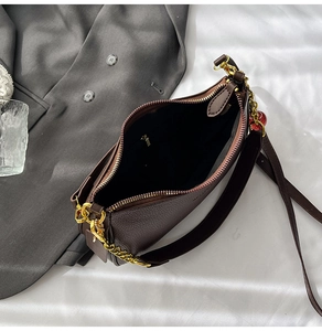 Detailed macro view of litchi-grain leather texture with gold chain on dark brown bag