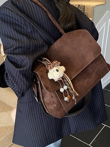 Deep brown suede crossbody bag with cute plush dog charm shown on shoulder