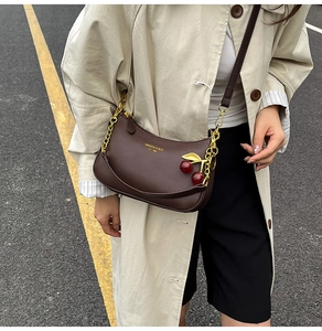 Detail of a dark brown lychee leather crescent bag with a decorative cherry charm