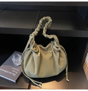 Detail einer olivgrünen Cord-Handtasche mit Kordelzuggriff auf modernem Display-Ständer