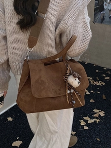 Brown suede crossbody bag with plush dog charm and canvas strap shown on a street