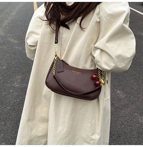 Detail of coffee leather hobo bag with gold chain and a cute red cherry pendant accessory