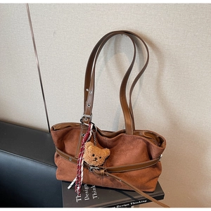 Détail d'un cabas en daim marron foncé avec sangle décorative et breloque ours