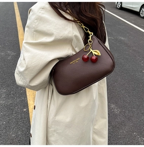 Detail of dark brown lychee leather underarm bag with gold chain and cherry charms
