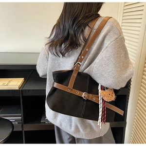Détail du sac cabas en daim noir avec lanières en cuir, breloque ours et pompon tressé
