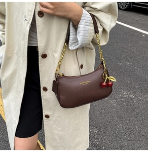 Detail of dark brown lychee leather underarm bag with gold chain and cherry charm