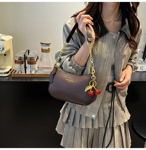 Detailed view of dark brown leather underarm bag with gold chain and cherry charm detail