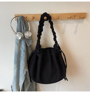 Details einer schwarzen Cord-Schultertasche mit Faltenriemen und Kordelzugverschluss