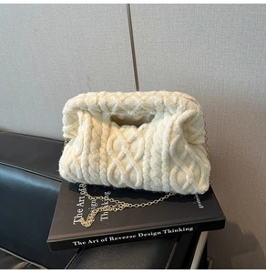 Detail of cream cable knit pouch bag with delicate gold chain strap on design book