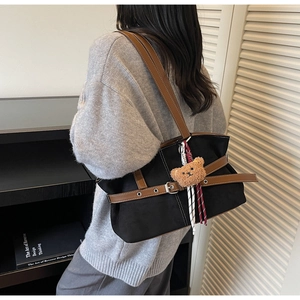 Détail du sac cabas en toile noire avec lanières en cuir et breloque ours en peluche