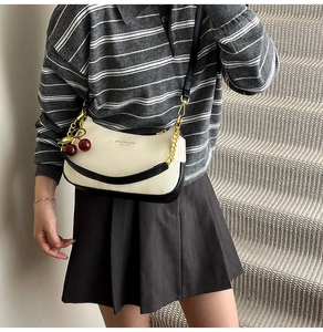 Close-up of white lychee leather chain bag with black piping and cherry charm detail