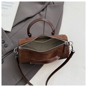 Overhead view of a brown suede cylinder bag with leather straps on a stylish gray blazer