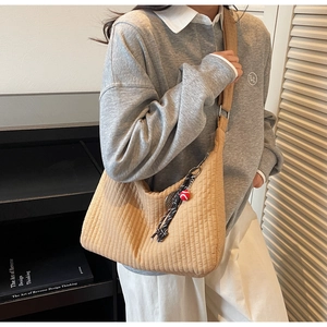 Detail of beige crescent crossbody bag with pleated texture and sporty red ball charm