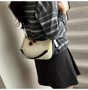 Detail of cream leather hobo bag with gold chain and red cherry charms on strap