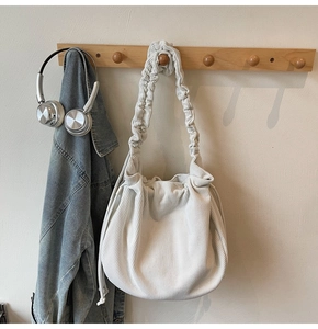 Detail der cremefarbenen Cord-Schultertasche mit gerafftem Riemen am Holzsockel