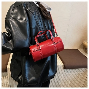 Close-up of a glossy red cylinder bag featuring metallic buckles and leather texture