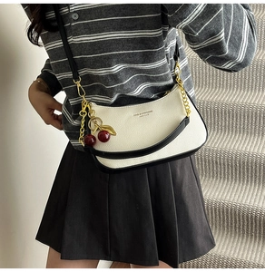 Detail of white half-moon bag with black edges, cherry charm and metal chain strap