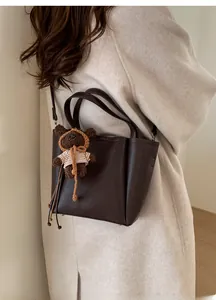 Detail view of dark brown bucket bag with a cute bear pendant on a beige coat