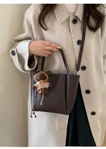 Detail of dark brown pebble leather tote bag with a knitted bear charm and long strap