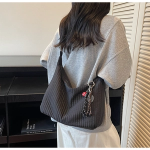 Détail d'un sac cabas noir avec matelassage vertical et breloque cœur sur une épaule