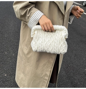 Close-up of white chunky knit handbag with 3D cable pattern held by a model in a trench coat